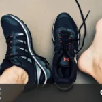 یک جفت کفش ورزشی مشکی که یک لنگه آن در پای فرد است و لنگه دیگر روی زمین