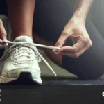 فردی که روی زمین نشسته و بند کفش خود را می بندد